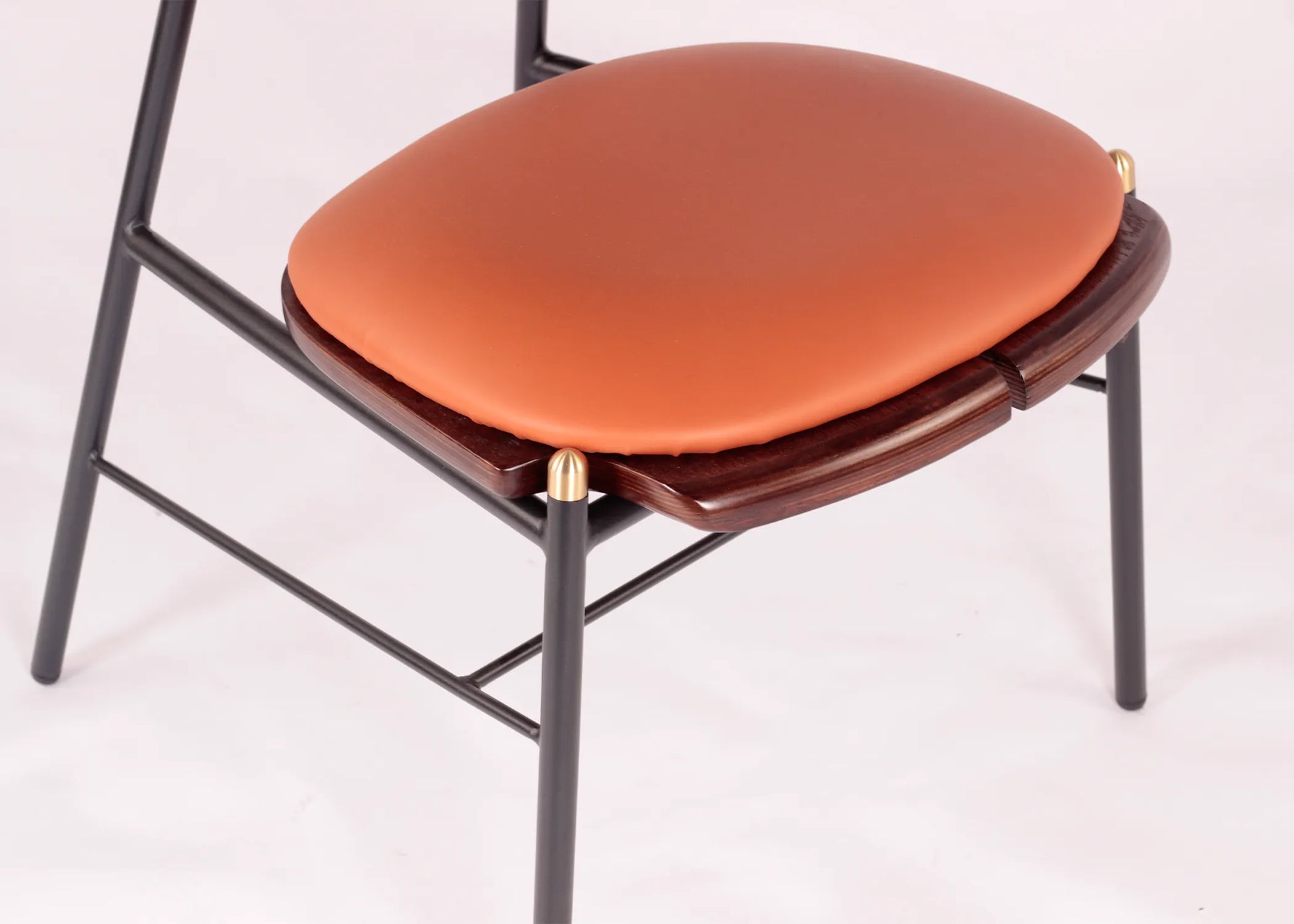 Silla Mocán con estructura metálica negra y asiento acolchado en tono terracota sobre base de madera de fresno.