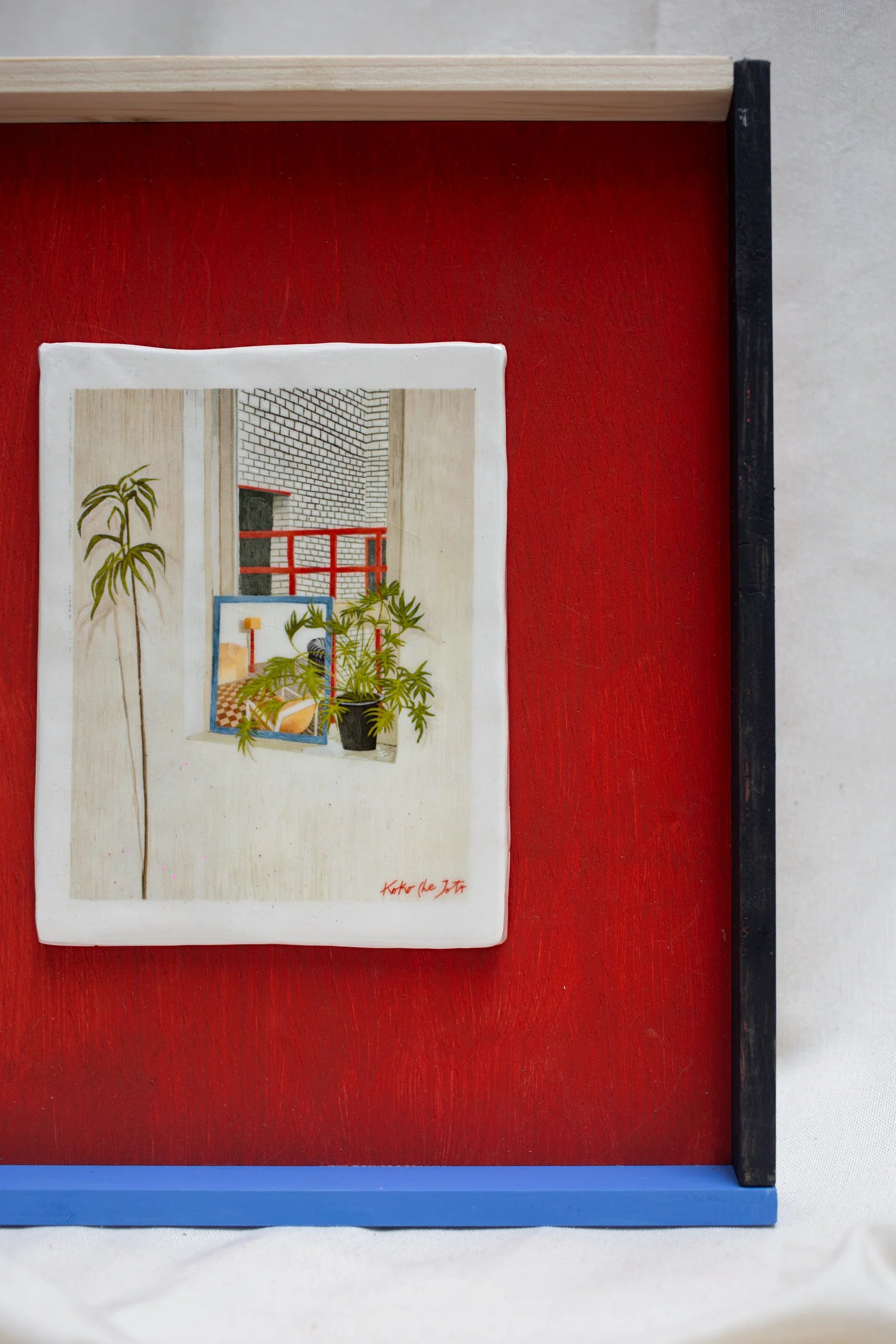 METACUADRO" // Cuadro de Cerámica con plantas en ventana, marco con detalles en rojo, azul y negro sobre fondo claro.