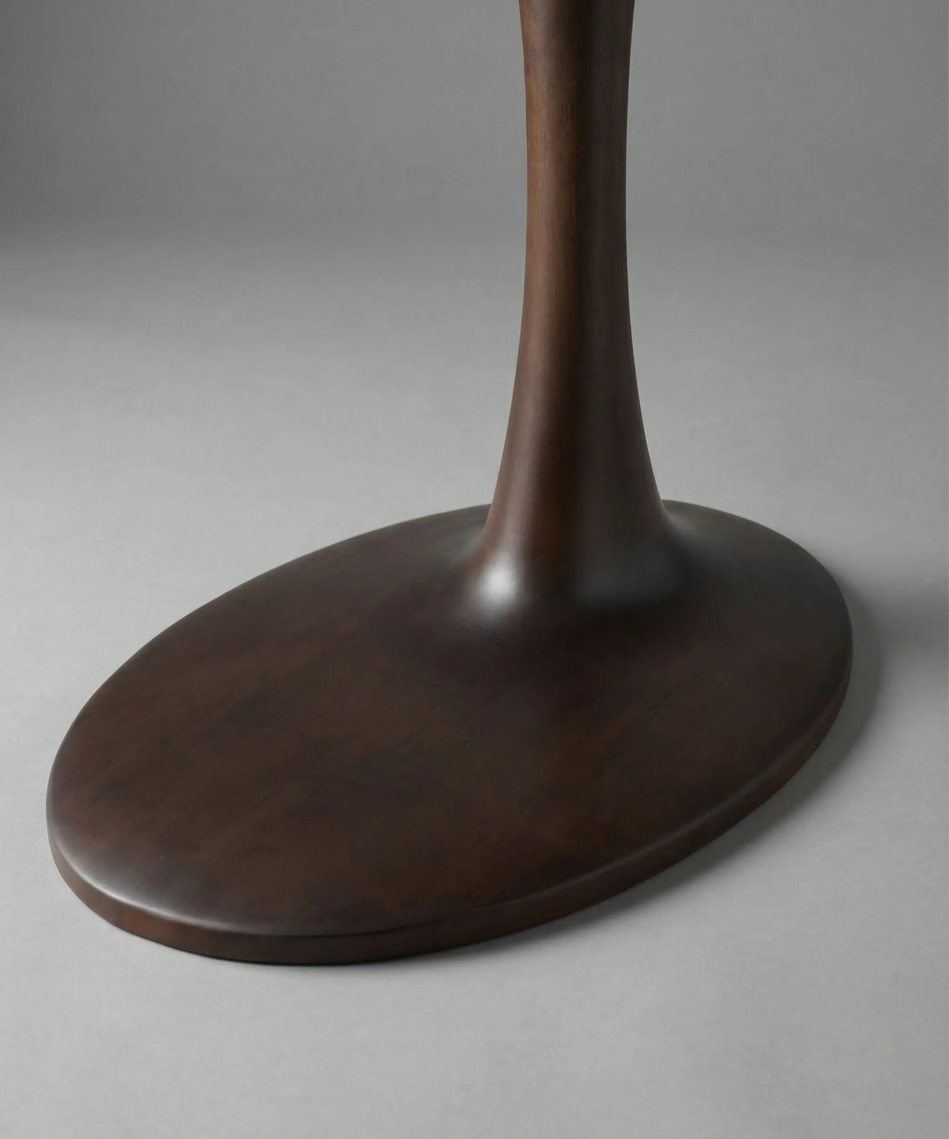 Mesa auxiliar Brisa con base en madera de fresno nogal oscuro, diseño contemporáneo y perfil escultórico elegante.