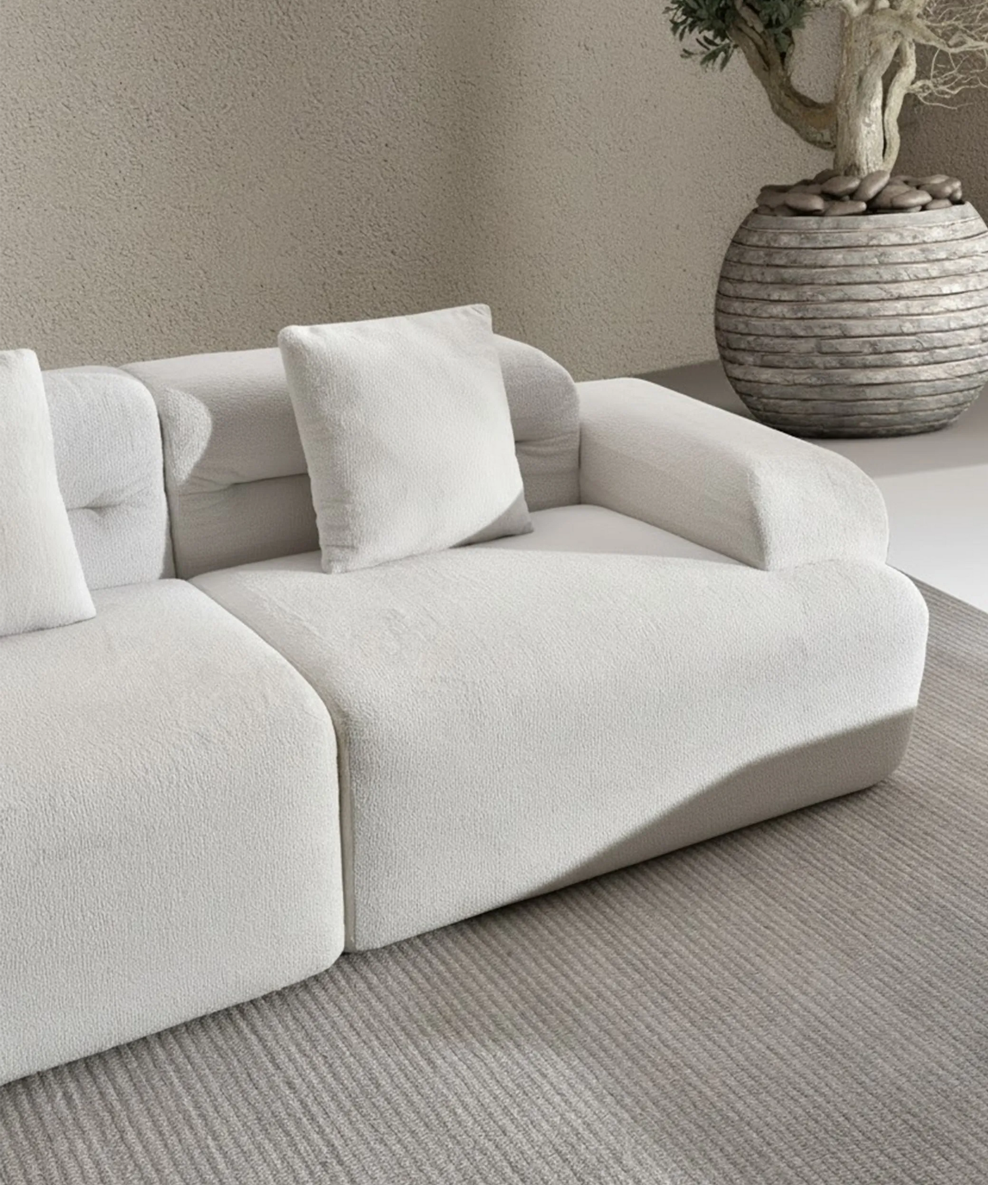 Sofá modular Haría en tono claro con diseño minimalista y cojines, sobre alfombra gris junto a maceta decorativa.