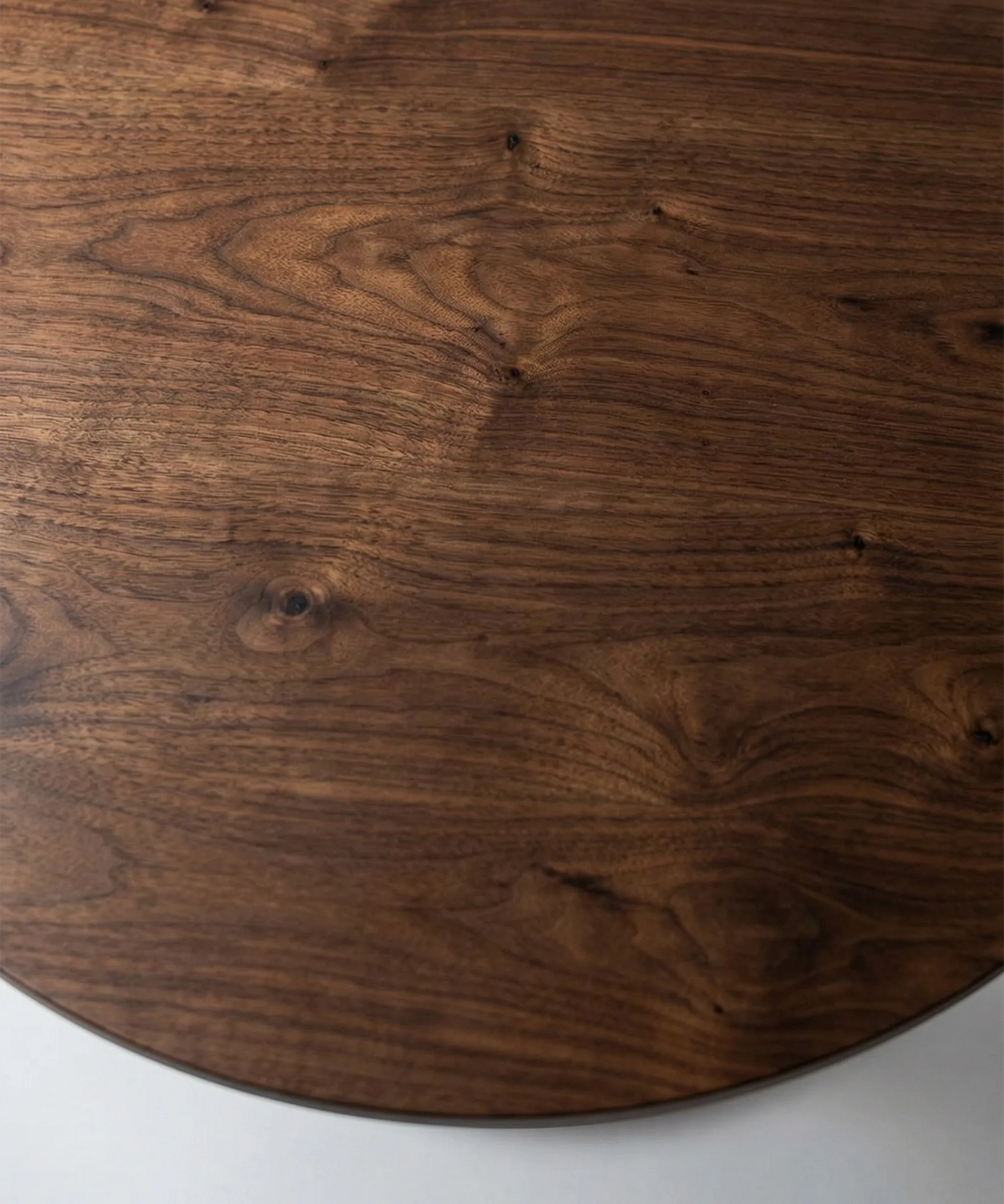 Mesa Vegueta redonda en madera de fresno con acabado en nogal oscuro, diseño contemporáneo y textura natural.